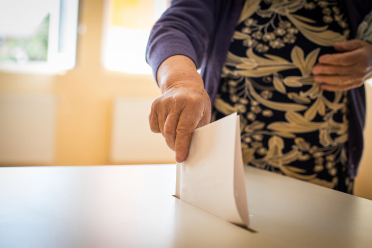 Color image of a person casting a ballot at a polling station, during elections.