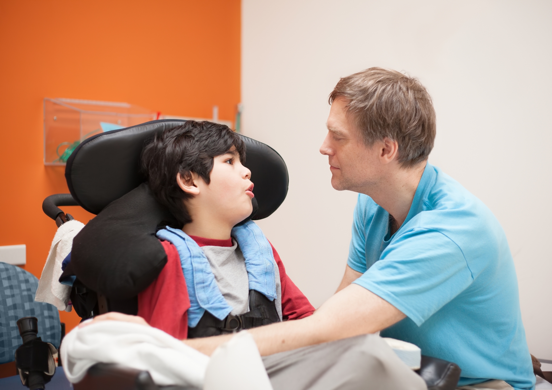 Disabled little boy in wheelchair talking with father in hospital room